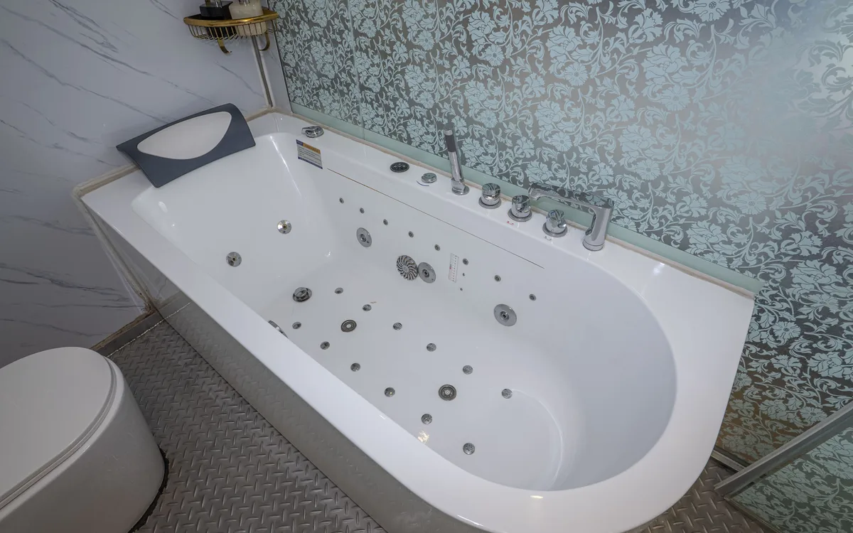 Bồn tắm trắng có vòi massage đặt cạnh tường gạch hoa văn xanh trong phòng tắm Sao Việt Hotel