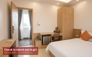 Check in check out là gì – ảnh minh hoạ phòng giường đôi ga trắng nhìn từ cửa ra vào, kèm tiêu đề bài viết