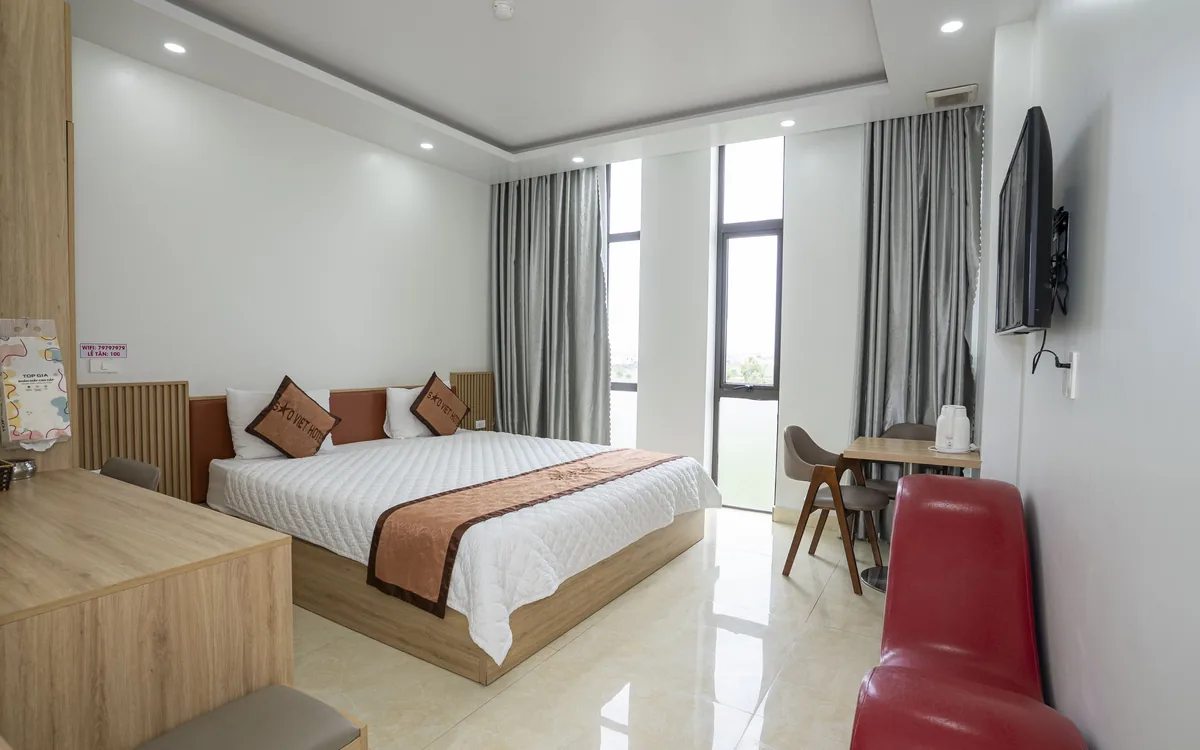 Dịch vụ dọn phòng khách sạn – phòng giường đôi ga trắng, rèm xám, bàn ghế và ghế sofa đỏ tại Sao Việt Hotel An Lão