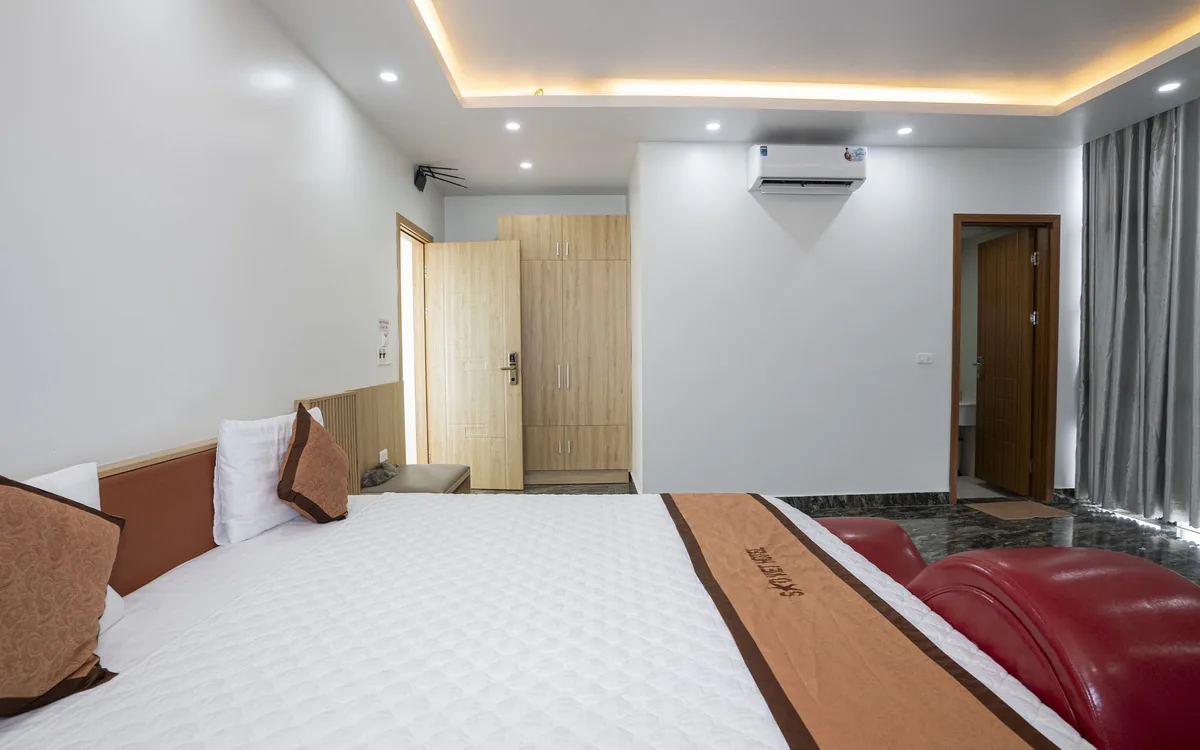 Giường đôi ga trắng có khăn trải giường nâu vàng, ghế sofa đỏ dáng cong và đèn hắt trần trong phòng Sao Việt Hotel An Lão