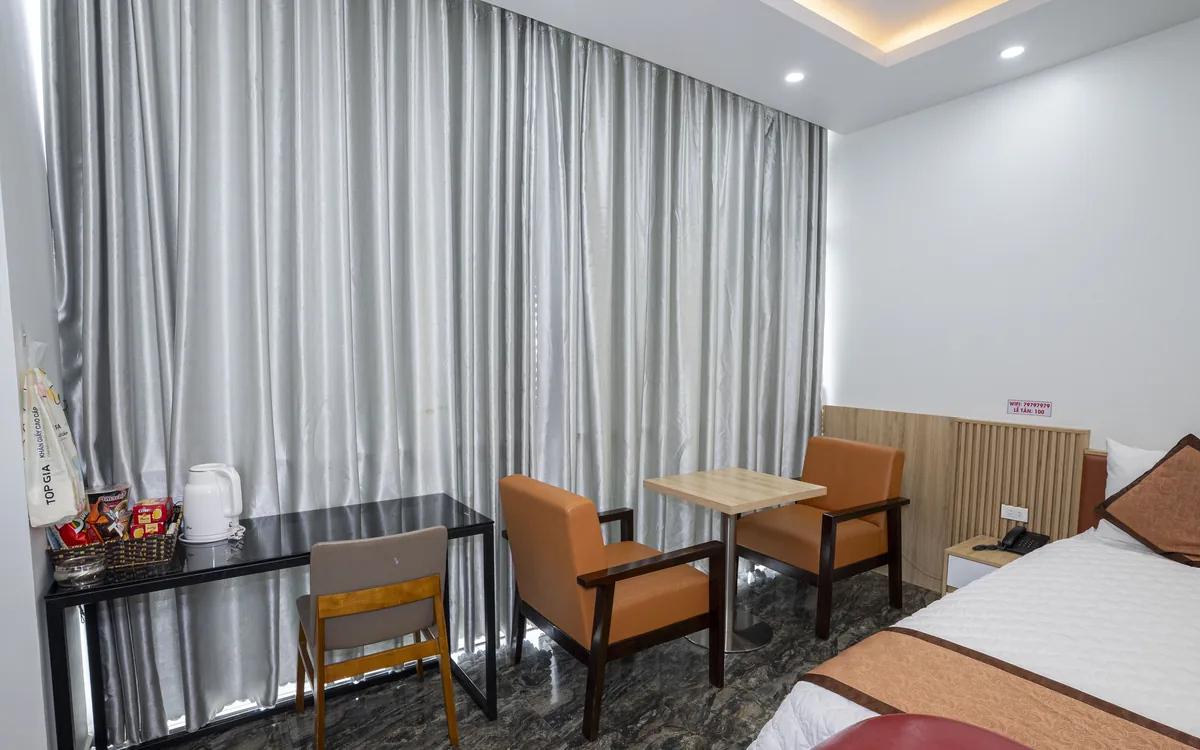 Góc bàn trà có ấm siêu tốc, khay đồ uống, cặp ghế gỗ đệm cam bên rèm cửa sổ tại Sao Việt Hotel