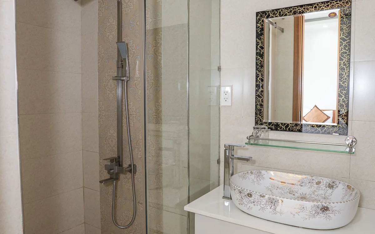 Góc lavabo có gương khung hoa văn và vòi sen vách kính trong phòng tắm Sao Việt Hotel
