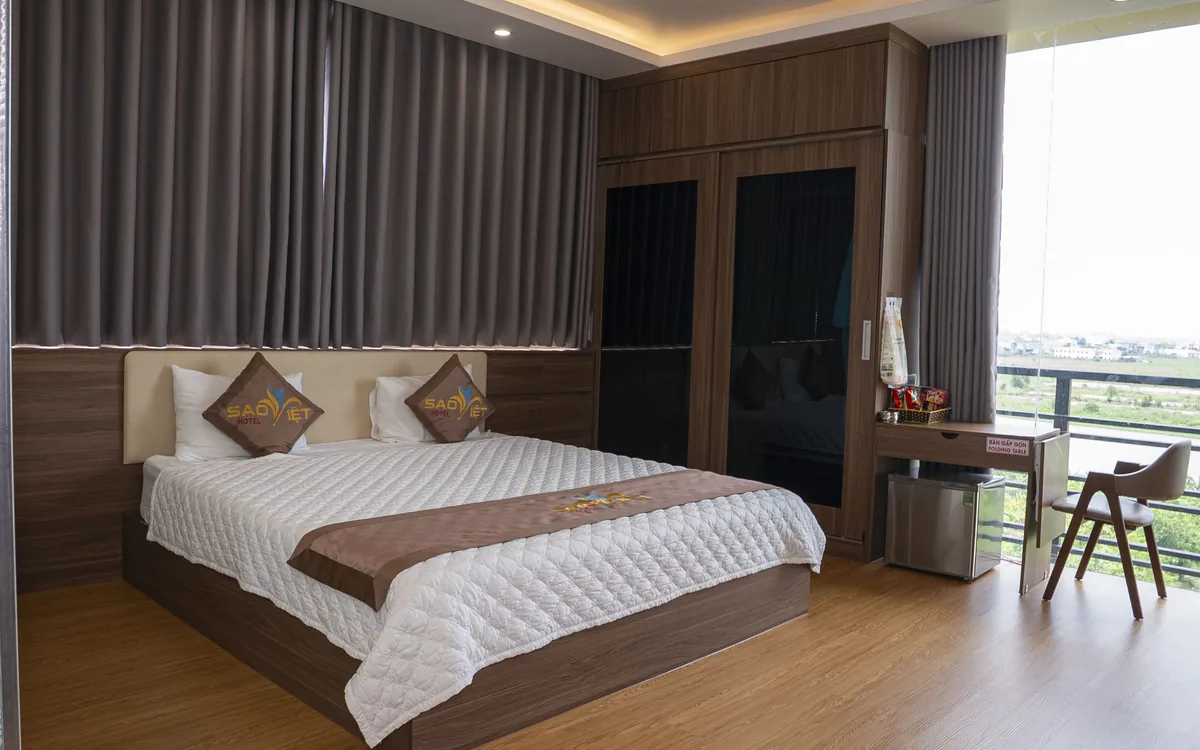 Phòng ốp gỗ tại Sao Việt Hotel có giường đôi, bàn làm việc cạnh cửa kính nhìn ra cánh đồng