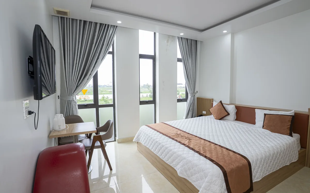 Phòng giường đôi có dãy cửa sổ kính nhìn ra cây xanh, TV treo tường và ghế đỏ tại Sao Việt Hotel