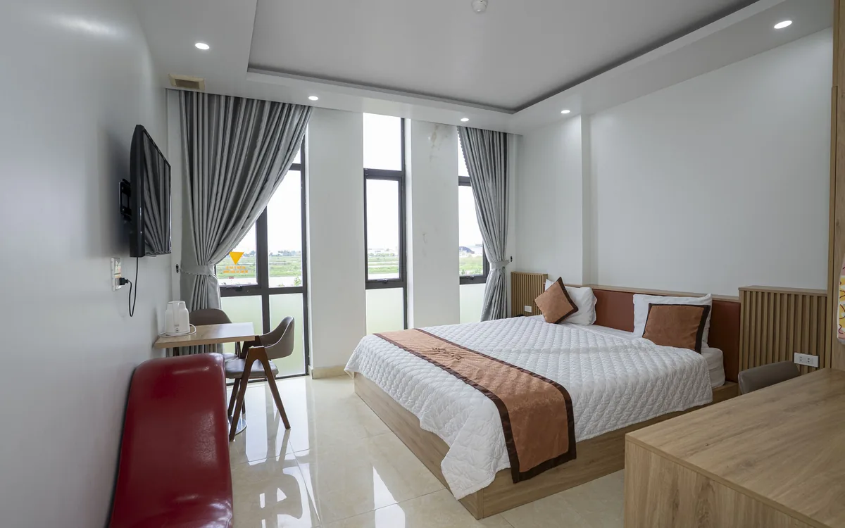 Phòng giường đôi tại Sao Việt Hotel có dãy cửa kính cao nhìn ra cánh đồng, rèm xám và TV treo tường