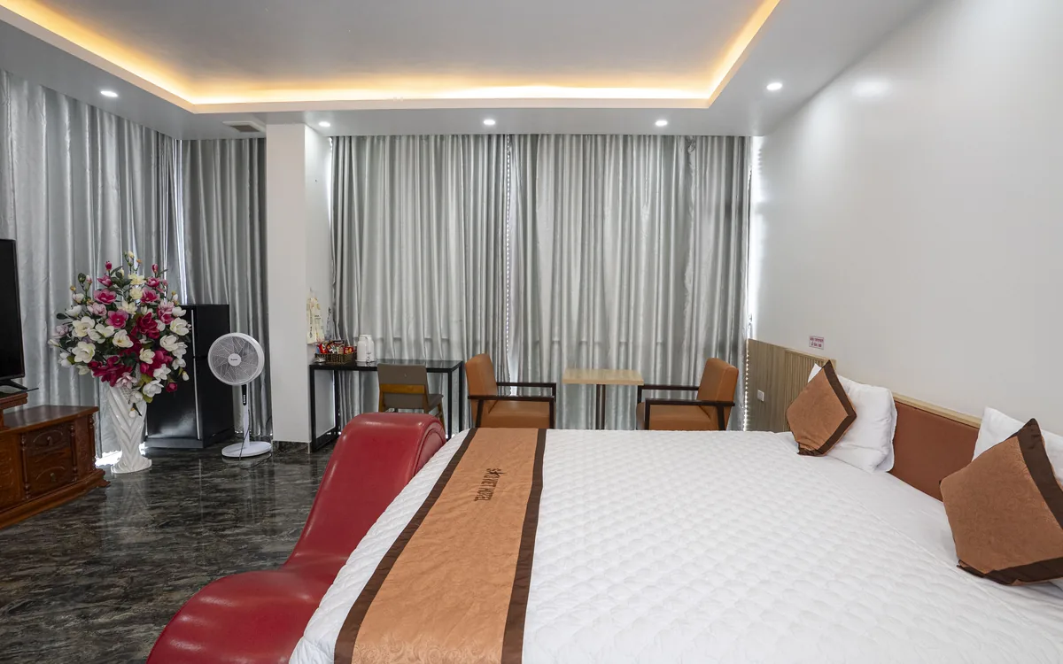 Phòng sàn đá tối với ghế sofa đỏ dáng cong, giường đôi, bình hoa, quạt cây và điều hoà tại Sao Việt Hotel An Lão