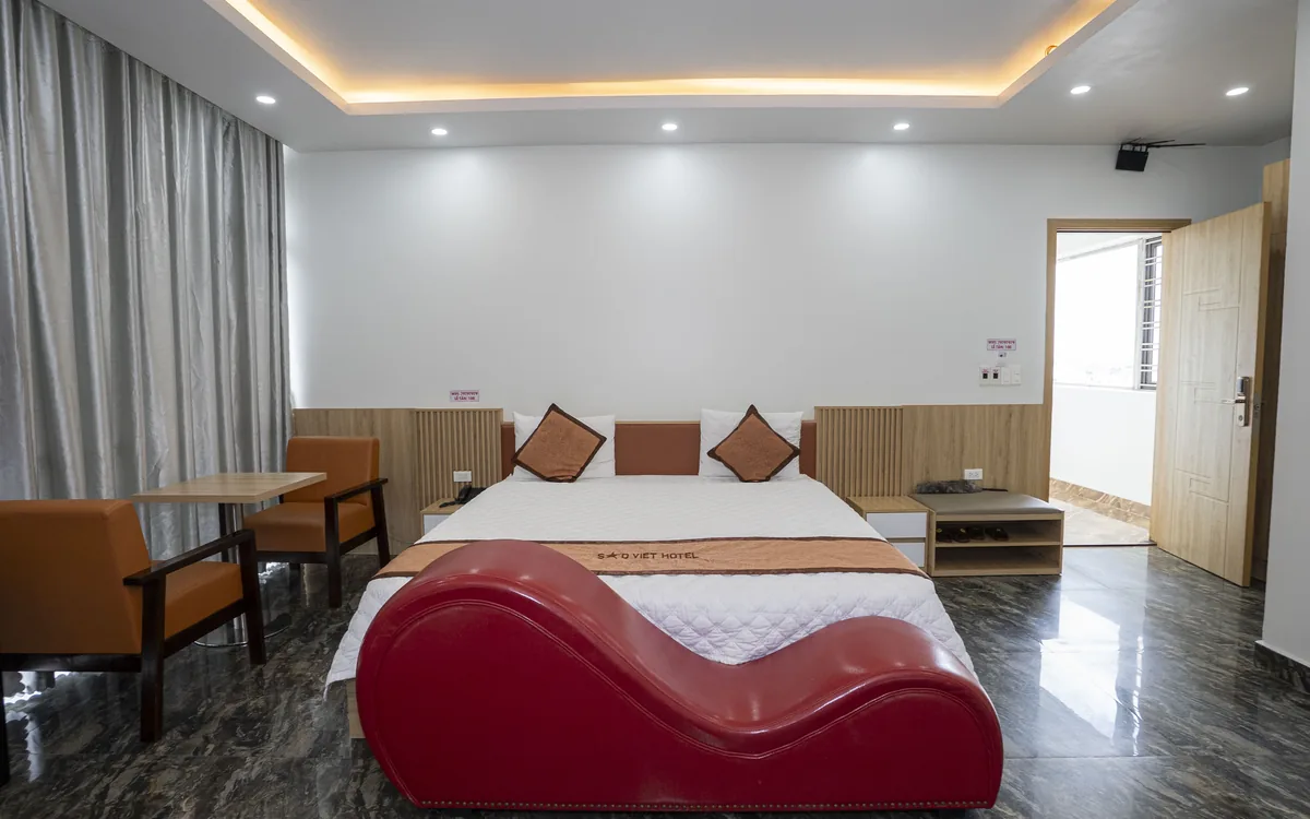 Phòng sàn đá tối, đèn hắt trần, ghế sofa đỏ dáng cong, giường đôi và TV lớn tại Sao Việt Hotel