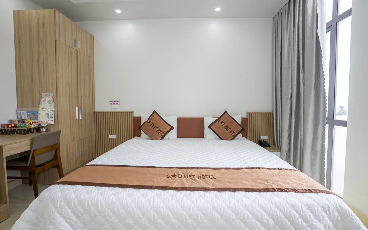 Phòng sáng với giường đôi ga trắng, tủ gỗ và bàn làm việc nhỏ tại Sao Việt Hotel