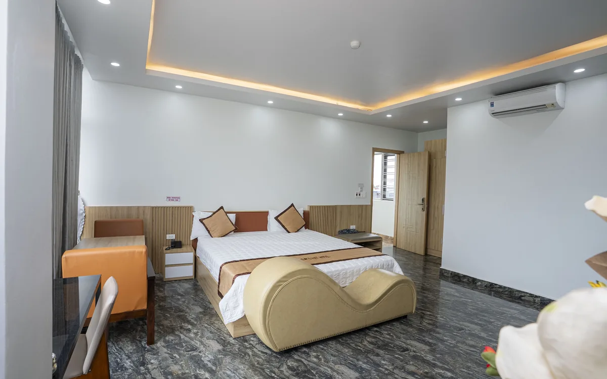 Phòng giường đôi sàn đá tối nhìn qua chậu hoa lan tiền cảnh, đèn hắt trần sáng tại Sao Việt Hotel