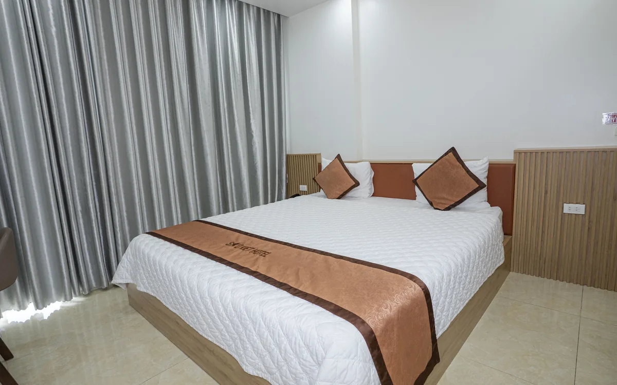 Phòng giường đôi ga trắng, gối nâu đỏ, TV treo tường và rèm xám tại Sao Việt Hotel