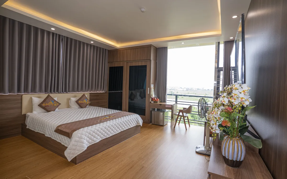 Phòng ốp gỗ sàn gỗ với giường đôi, bình hoa và cửa kính ra ban công tại Sao Việt Hotel An Lão