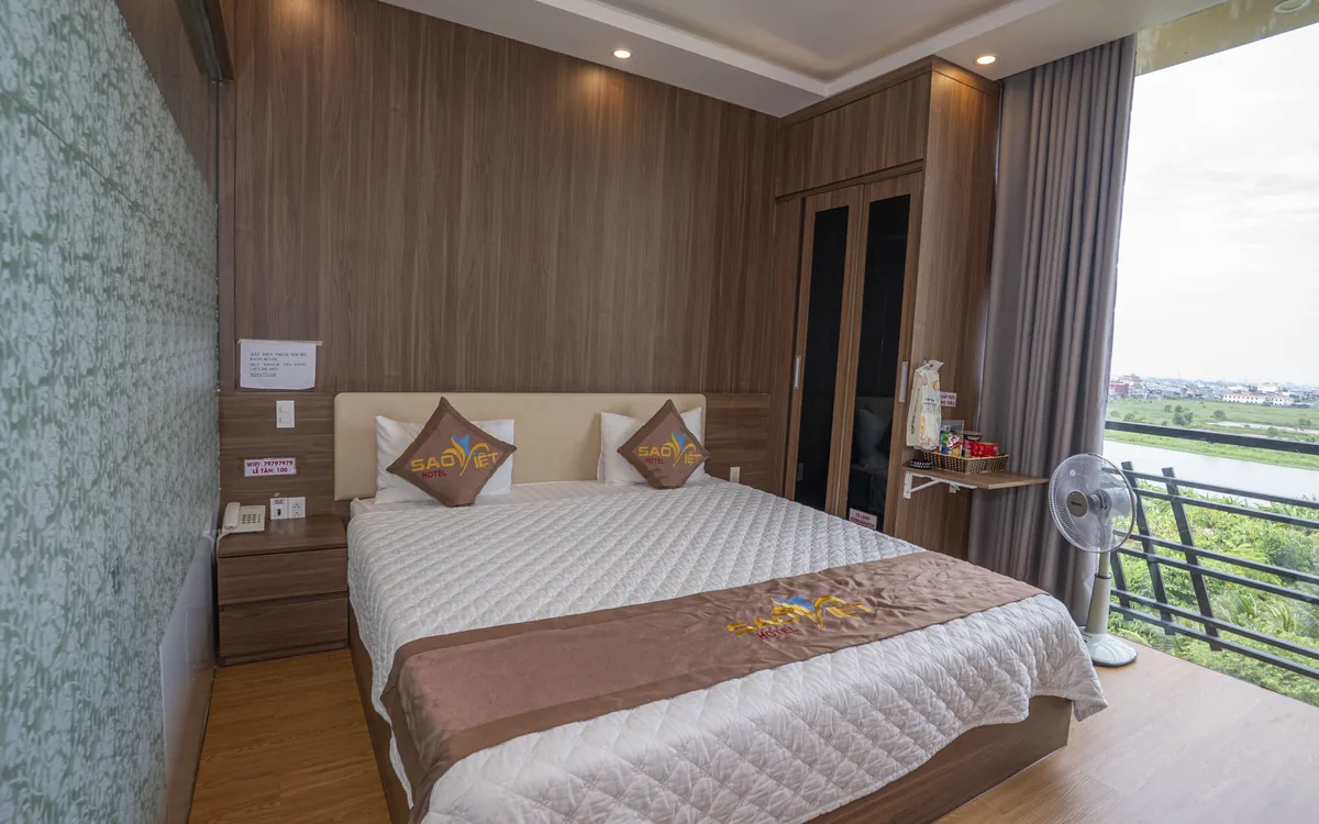 Phòng nội thất gỗ với giường đôi, TV lớn và ban công kính tại Sao Việt Hotel An Lão