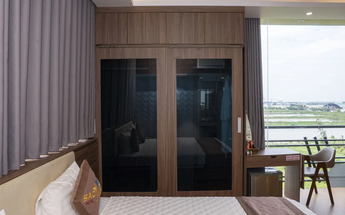 Phòng ốp gỗ tối với tủ kính đen, giường đôi và cửa kính lớn nhìn ra cánh đồng tại Sao Việt Hotel An Lão