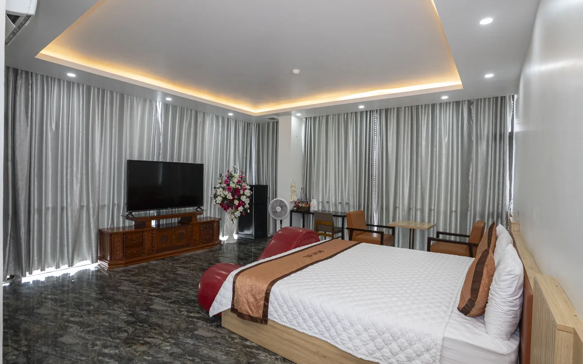 Phòng lớn sàn đá tối, đèn LED hắt trần, giường đôi ga trắng đối diện TV trên kệ gỗ tại Sao Việt Hotel An Lão