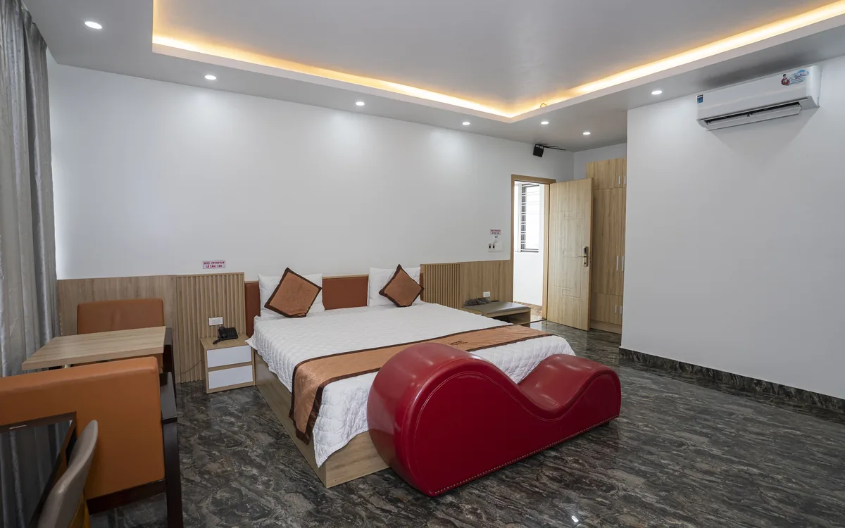 Phòng lớn sàn đá tối với giường đôi, ghế sofa đỏ dáng cong, bàn ghế, điều hoà và đèn hắt trần tại Sao Việt Hotel An Lão