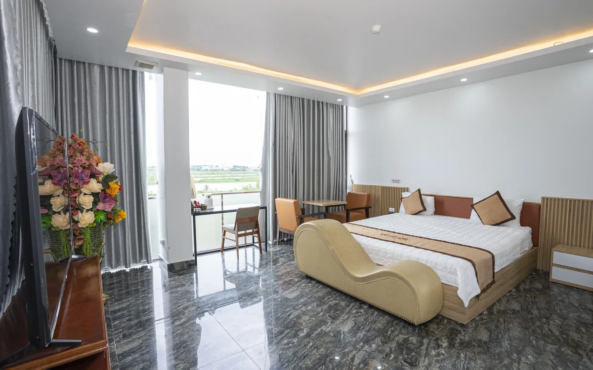 Phòng lớn sàn đá tối tại Sao Việt Hotel An Lão với giường đôi, ghế thư giãn và cửa kính ra ban công