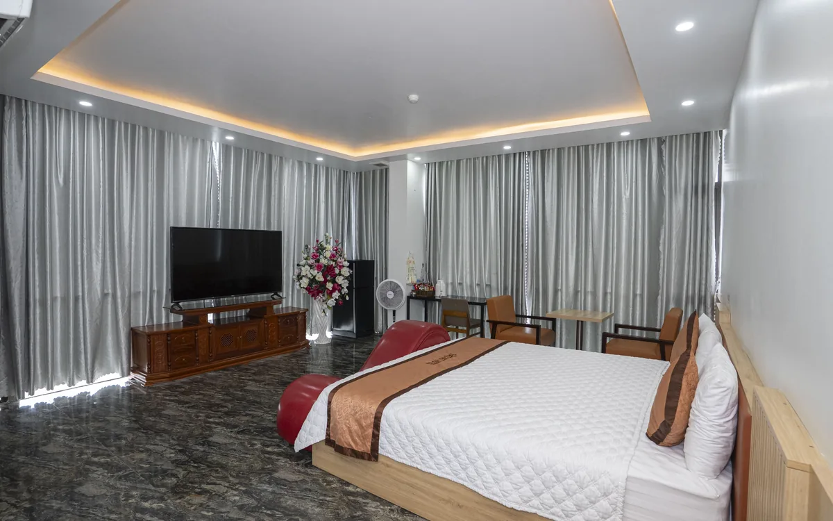 Phòng rộng sàn đá với 1 giường đôi lớn, TV và rèm xám tại Sao Việt Hotel