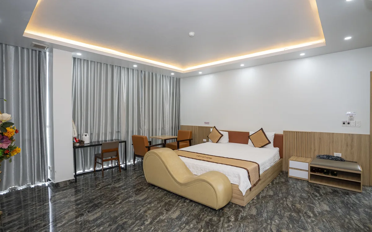 Phòng single là gì – phòng lớn sàn đá tối, đèn hắt trần, 1 giường đôi và ghế thư giãn màu be tại Sao Việt Hotel