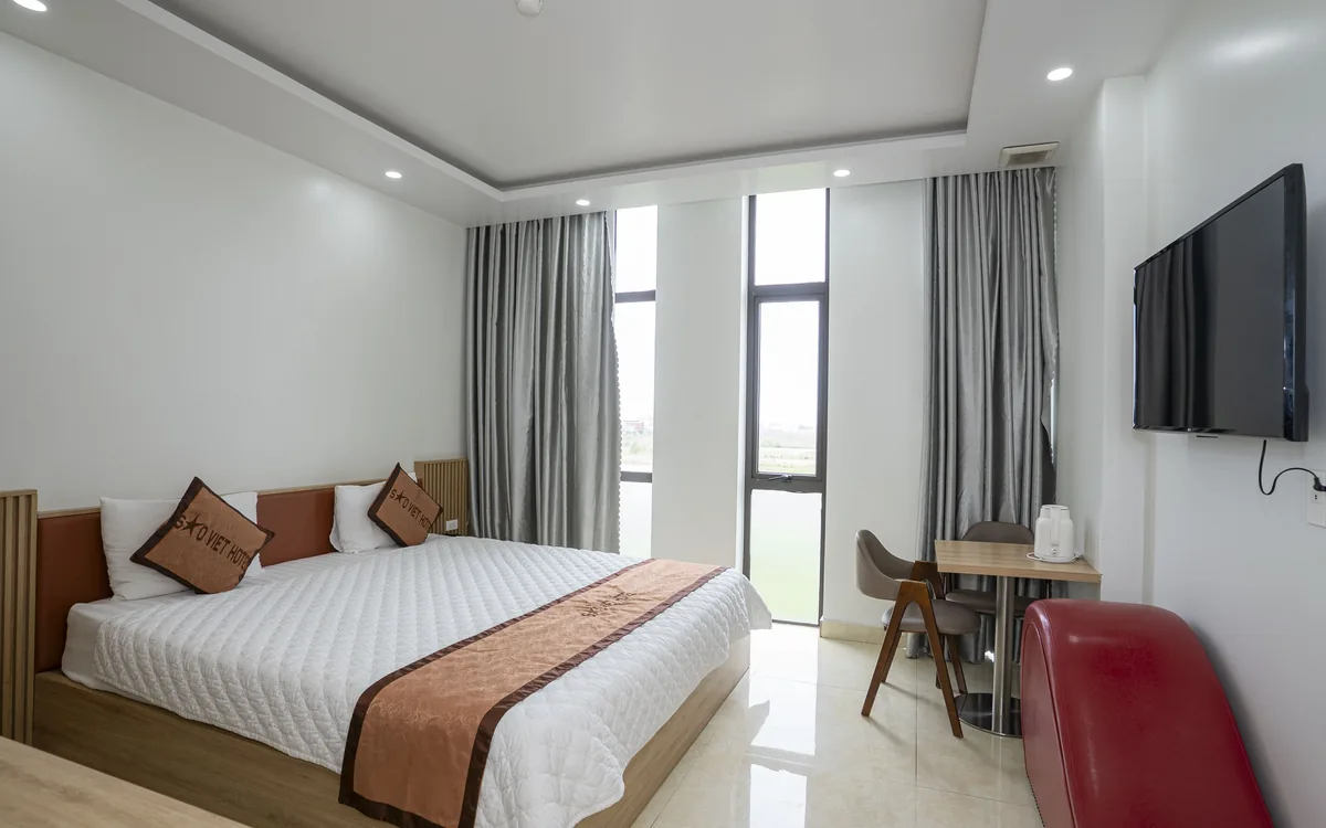 Phòng Standard double ở An Lão – giường đôi, TV, bàn ghế cạnh cửa sổ nhìn ra cây xanh tại Sao Việt Hotel