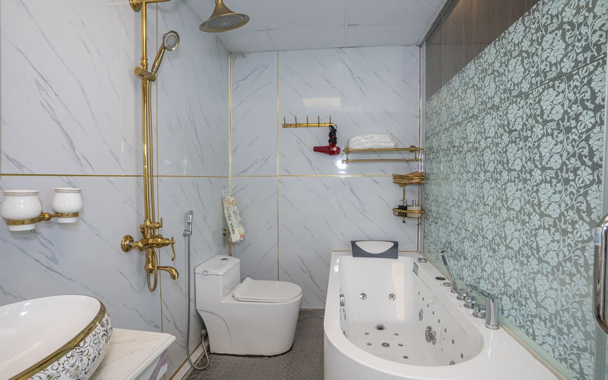 Phòng tắm gạch vân đá trắng với bồn tắm, vòi sen mạ vàng và bồn cầu tại Sao Việt Hotel