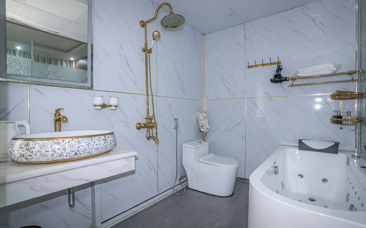 Phòng tắm gạch vân đá trắng với lavabo, vòi sen mạ vàng, bồn cầu và bồn tắm tại Sao Việt Hotel