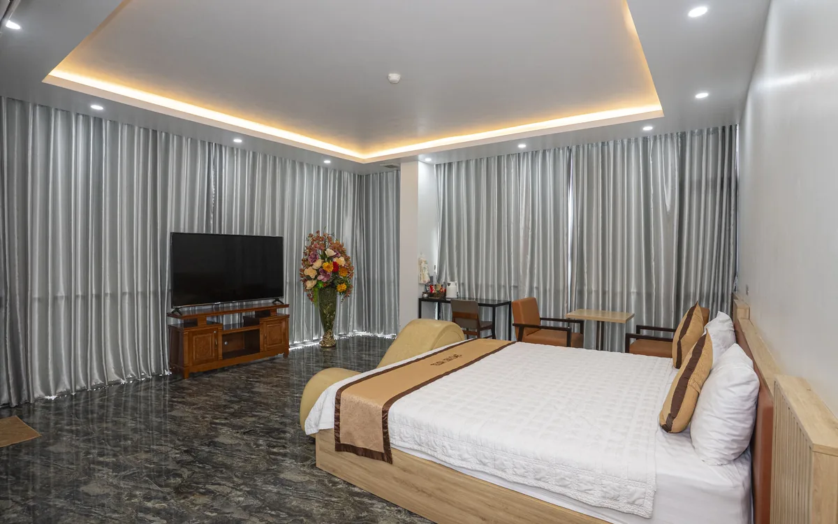 So sánh hạng phòng ở An Lão – phòng lớn sàn đá vân tối, đèn hắt trần, 1 giường đôi, ghế be dáng cong và TV lớn tại Sao Việt Hotel