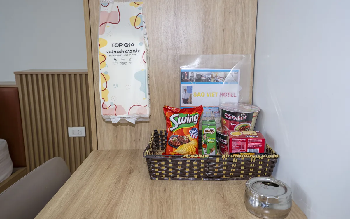 Giỏ đồ ăn nhẹ và đồ dùng cá nhân đặt sẵn trên bàn gỗ trong phòng Sao Việt Hotel