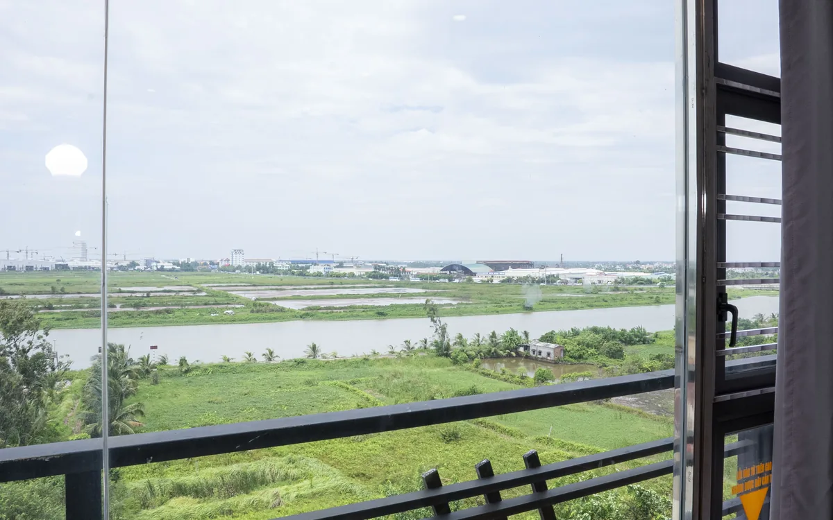 View từ cửa sổ khách sạn ở An Lão – sông, cánh đồng xanh và nhà xưởng phía xa nhìn qua lan can tại Sao Việt Hotel